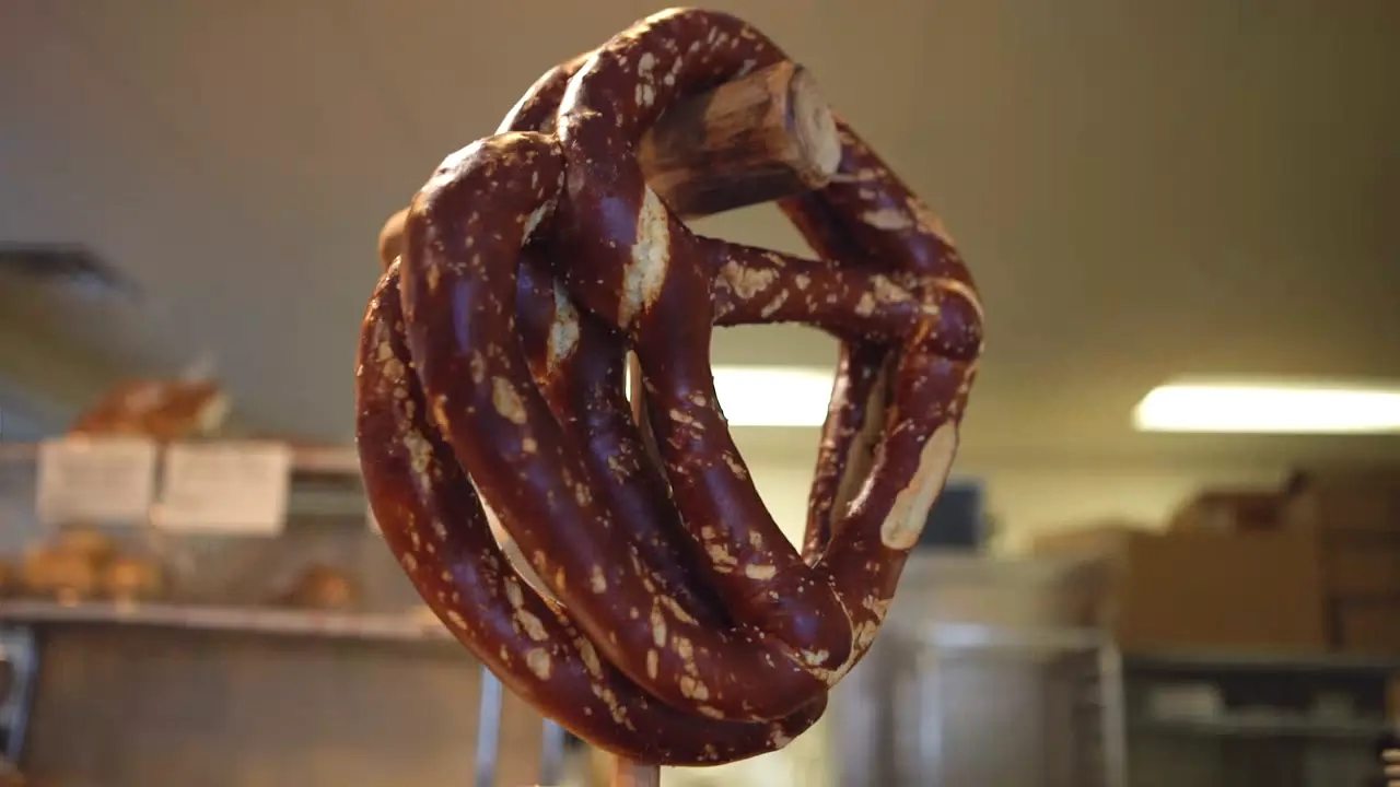 A dark, glossy pretzel held up in the bakery
